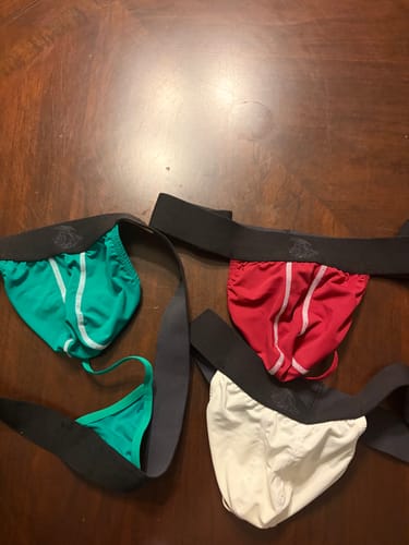 Reviewer's three pairs of Nylon Mesh Thongs in crimson, green, and bone laid out on a wooden table.