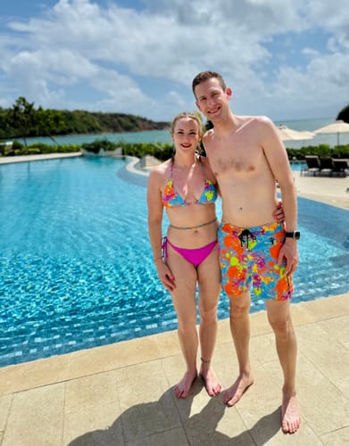 Customer and partner wearing colorful matching swimsuits by a resort pool.