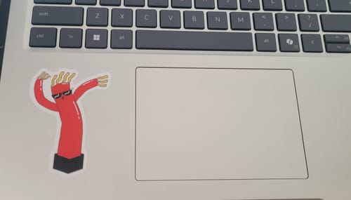 Customer's red wacky inflatable tube sticker applied to a silver laptop next to the trackpad.