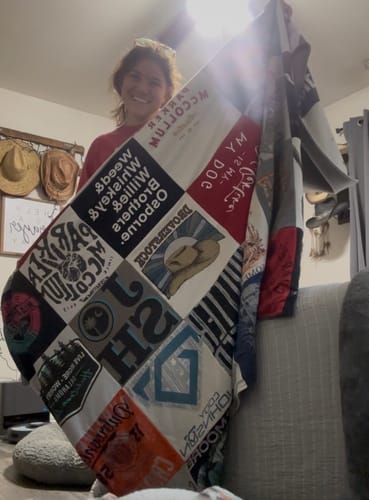 A happy reviewer holds up their large, custom Premium T Shirt Quilt, showing the different t-shirt designs.