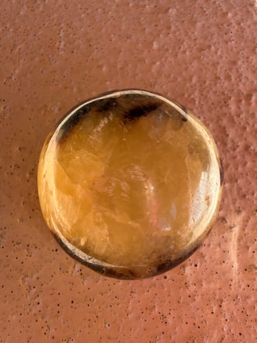 Reviewer's close-up of the round, honey-colored crystal palm stone with dark inclusions on a textured surface.
