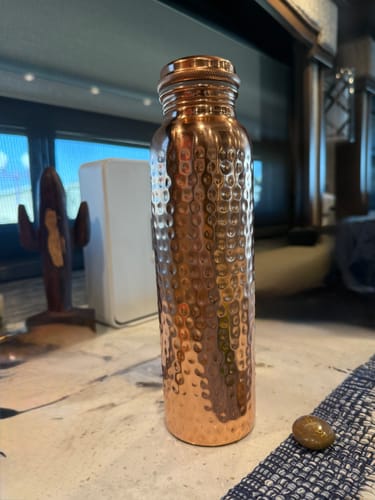 Customer's hand-hammered pure copper water bottle standing on a countertop, showing the textured finish.