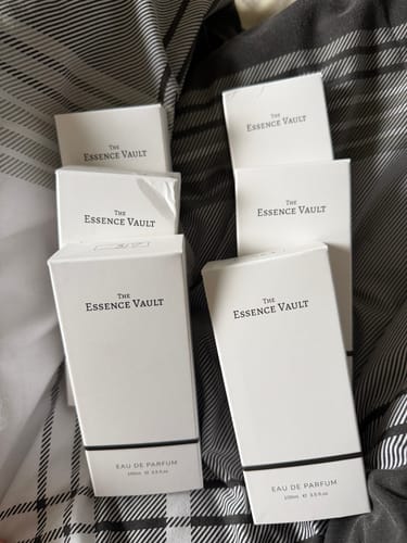 Customer showing several white 'The Essence Vault' perfume boxes arranged on a striped surface.