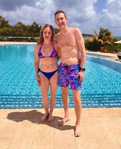 Customer and partner by a pool wearing matching Neon Orchid Magenta swim trunks and a bikini top.