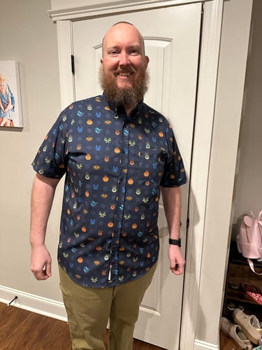 Reviewer wearing the 'Fiery Faces' short sleeve shirt, showing the subtle, colorful pattern of dragon faces on the dark fabric.