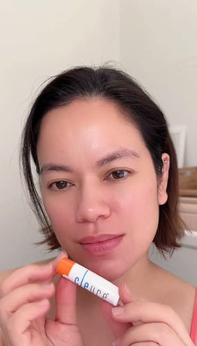 Reviewer holding the white tube of Lip Balm with Shea Butter with an orange cap.
