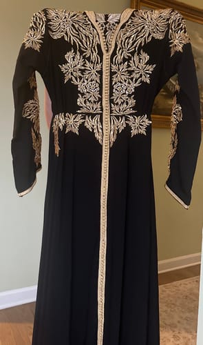 Customer's black Kaftan Jannet on a hanger, showing the elegant gold embroidery on the bodice and front.