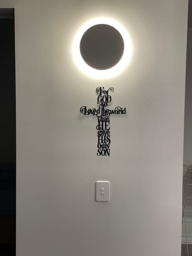 Customer's John 3:16 cross metal wall decor mounted on a light-colored wall, displayed beneath a modern circular light.
