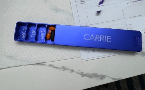 Reviewer's vibrant blue Weekly Case, personalized with an engraving and open to reveal the daily pill compartments.