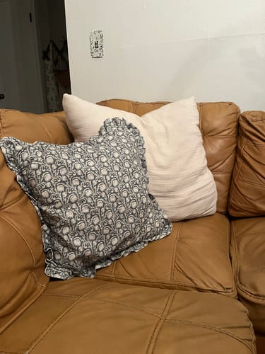 Customer's Quinn Ruffle pillow cover with a floral pattern and ruffled edge shown on a brown leather couch.