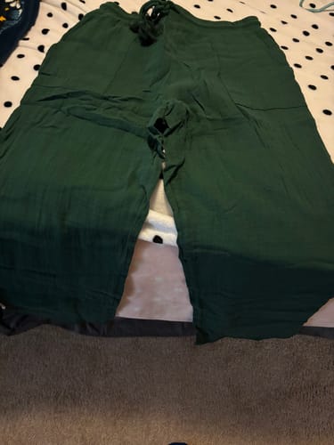 Customer's dark green, gauze tassel pants with a drawstring waist laid flat on a bed.