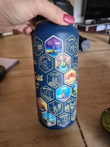 A customer's hand holding the blue World Explorer Bottle, showing several colorful destination stickers applied.