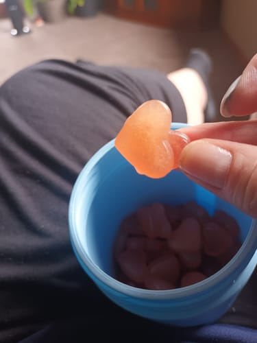 Customer holding a single, heart-shaped Peach gummy over a blue cup of more gummies.