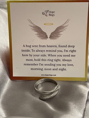 Reviewer's silver Hug From Heaven Ring with a 'DAD' engraving, shown in front of its comforting message card.