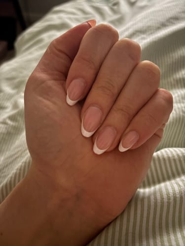 A reviewer's hand showing the almond-shaped Everyday Elegance press-on nails with a classic French manicure design.