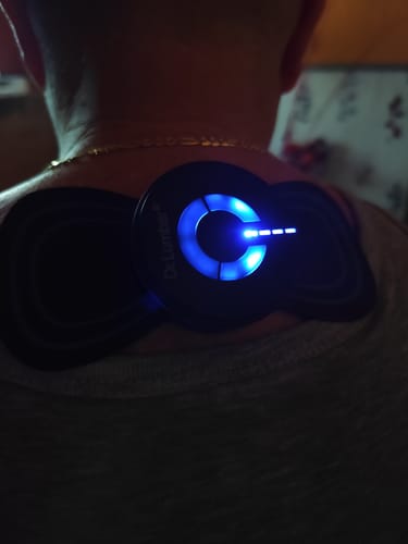 Vásárló a Vital Pulser Pro EMS Izomstimuláló Masszírozó Készüléket használja a nyakán, ami kék fénnyel világít.