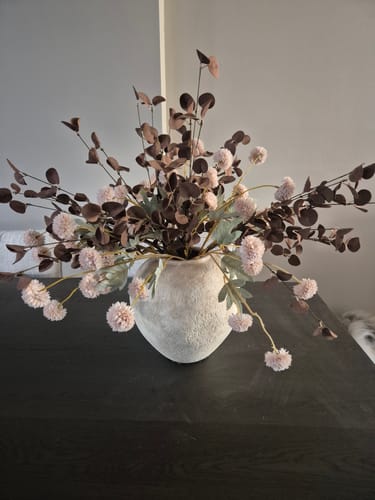 Recensent toont de beige Arda vaas, gevuld met een groot boeket op een donkere tafel.