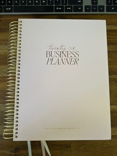 Customer's blush 2026 Business Planner with gold spiral binding, shown closed on a wooden desk.