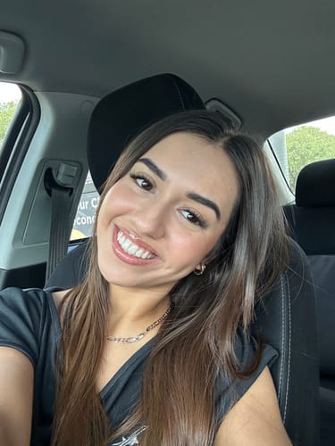 A customer smiling in a car, showing off her long, glamorous Infinaluxe lash extensions from the Complete Kit.