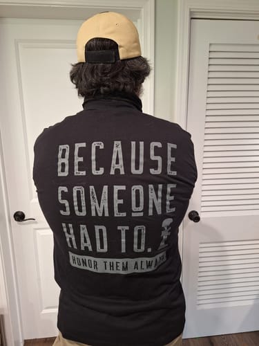 Reviewer from behind, wearing a black T.V.P. Elite Membership shirt with 'BECAUSE SOMEONE HAD TO.' printed on the back.