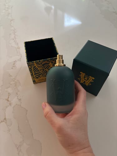Reviewer holding the dark teal Oud Bazaar perfume bottle with its box on a marble counter.