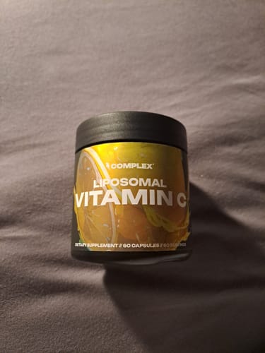 A customer's black tub of Liposomal Vitamin C with a yellow label, shown on a grey surface.