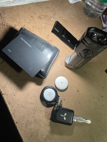 Reviewer's black SPOTMINDERS Tracking Card in a wallet, shown next to an Apple AirTag and car key on a desk.