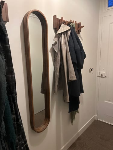 Recensent toont de by fonQ Pane spiegel met houten rand, hangend in de hal naast een kapstok.