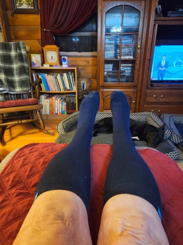 Reviewer wearing dark knee-high Performance Eucalyptus Compression Socks while relaxing with their feet up.