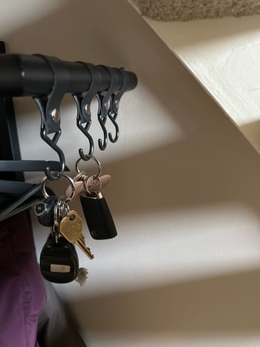 Klant toont de zwarte QUVIO ophanghaken met leren bandjes, gebruikt om sleutels op te hangen.