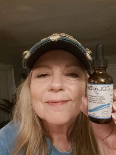 Smiling reviewer holding a brown dropper bottle of Colagene.