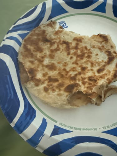 A customer's cooked Kawan Aloo Paratha on a paper plate, with a piece torn away to show the potato filling.