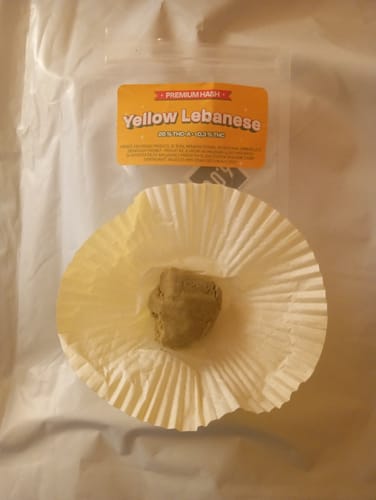 Customer's Yellow Lebanese THCA HASH displayed in a paper liner, with its packaging in the background.