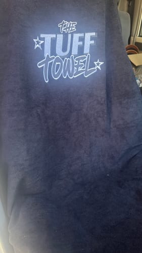 Close-up of a customer's black Waterproof Car Towel Seat Cover, showing the 'The Tuff Towel' logo.