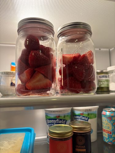 Customer's fresh strawberries stored in two glass mason jars inside a refrigerator after being sealed with the Mason Genie kit.