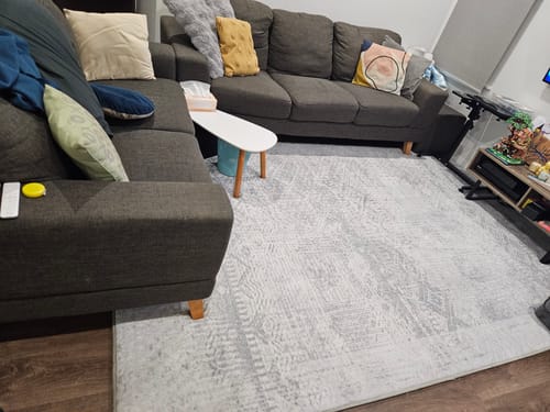 Customer's Silver Mist Mellow Mat laid out in a living room in front of a dark grey sectional sofa.