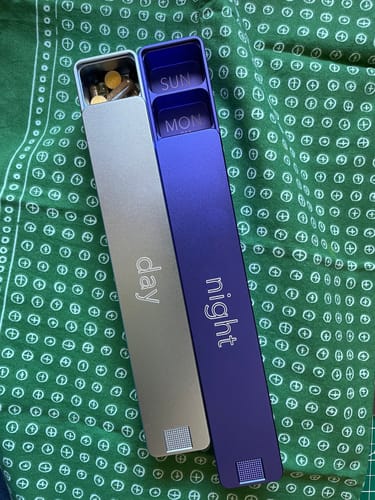 Reviewer's Weekly AM-PM Vitamin Case 2.0 showing the separate silver 'day' and purple 'night' cases on a green cloth.