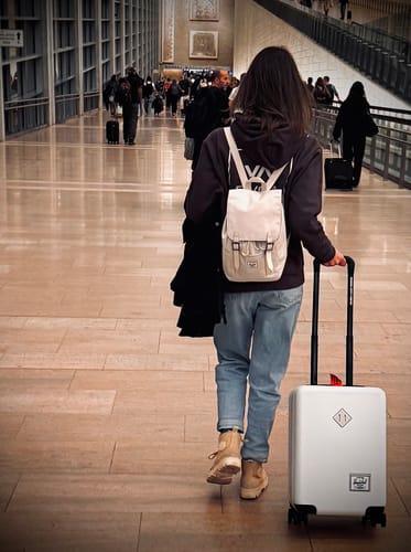 לקוחה הולכת בטרמינל עם תיק הגב הבהיר Retreat Mini ומזוודה.