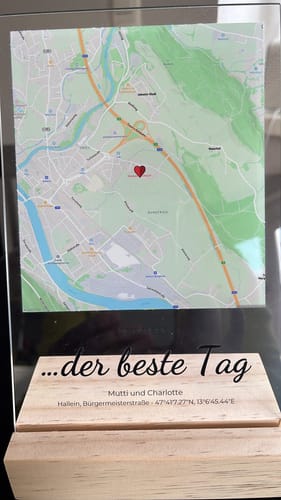 Kunde zeigt die personalisierte Acryltafel mit einer Karte, einer Herz-Markierung und einem Text auf dem Holzsockel.