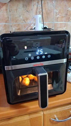 Client folosind air fryer-ul negru Novio StonePro, cu mâncare rumenită vizibilă în cuvă.