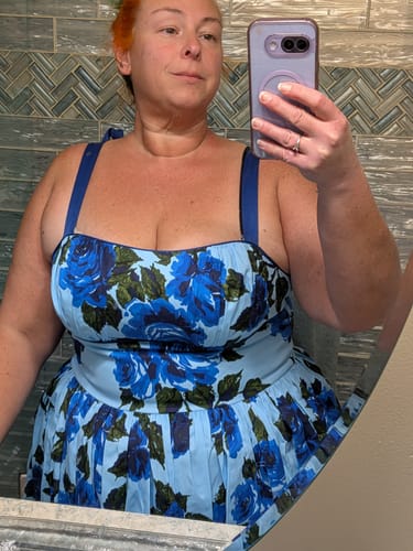 Reviewer taking a mirror selfie to show the fit of the blue rose print 1950s Swing Sundress.