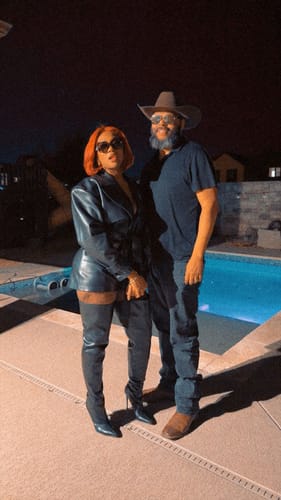 Reviewer wearing the black Vegan Leather Trench Romper with sunglasses and boots, standing by a pool at night.