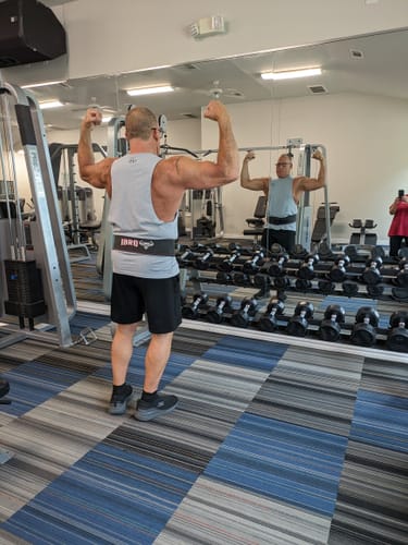 Reviewer in a gym flexing their biceps in front of a mirror, showing results from the V1X PRODIGY pre-workout.