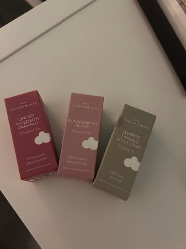 Klant toont de verpakking van de 'Onder moeders paraplu' olie naast twee andere Geurwolkje oliën op een witte ondergrond.