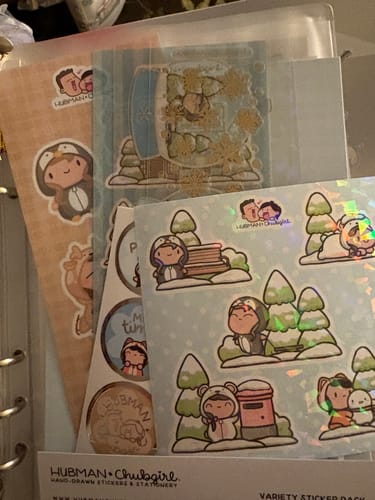 Reviewer's Winter Onesie Town Variety Sticker Pack fanned out, showing cute, iridescent sticker sheets inside a binder.