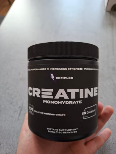 Reviewer holding a black tub of Complex Creatine Monohydrate in their hand.