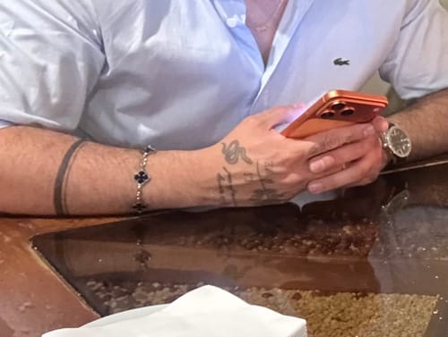 Cliente usando la Pulsera Black Clover en su muñeca tatuada mientras mira su teléfono.
