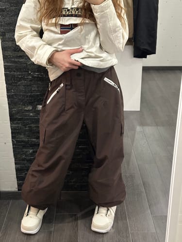 Reviewer wearing the baggy coffee snow pants indoors, showing the fit and white zippered front pockets.