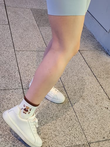 Reviewer wearing the Beary Latte socks with white sneakers on a tiled floor.