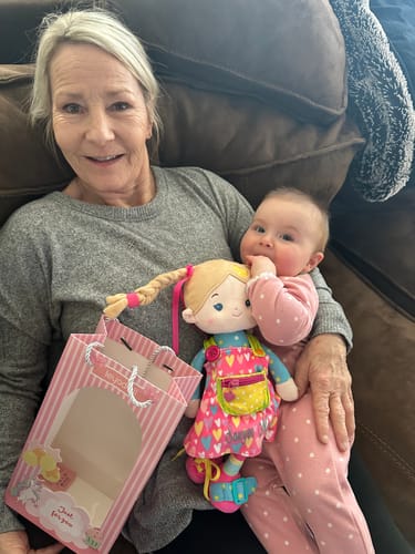 A customer's baby holding the colorful Sunnyheart Girl Montessori doll while sitting on a person's lap.